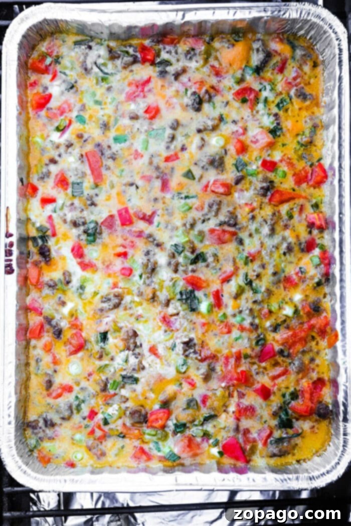 Hearty Smoked Queso Dip in a foil tray, brimming with melted cheese, vibrant red peppers, fresh green onions, and flavorful ground meat.