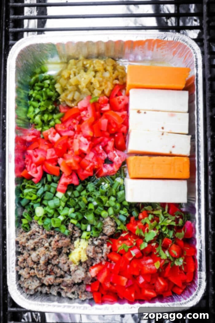 Meaty Smoked Queso Dip 6 Assembled smoked queso dip ingredients in a foil container on the grill, ready to meld into a savory appetizer.