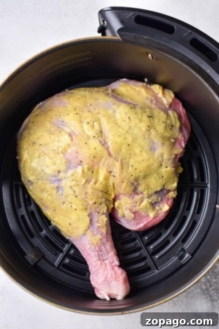 Succulent Turkey Leg Quarters 4 A raw turkey leg, perfectly coated with a yellow marinade, sits in an air fryer basket, ready to show you how to cook turkey legs and thighs to perfection.