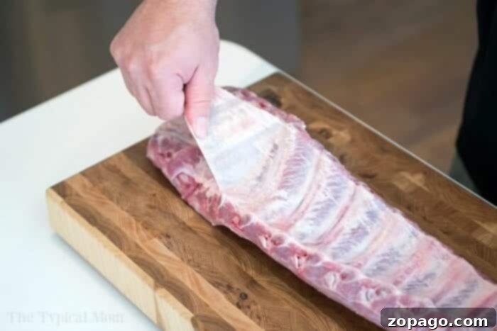 Fall-Off-The-Bone Slow Cooker Ribs 3 A hand demonstrating how to remove the membrane from a rack of ribs, a crucial step for tender results.