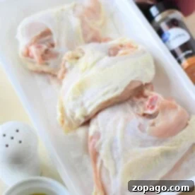 Raw bone-in chicken breasts ready for seasoning and cooking, next to spices and herbs.