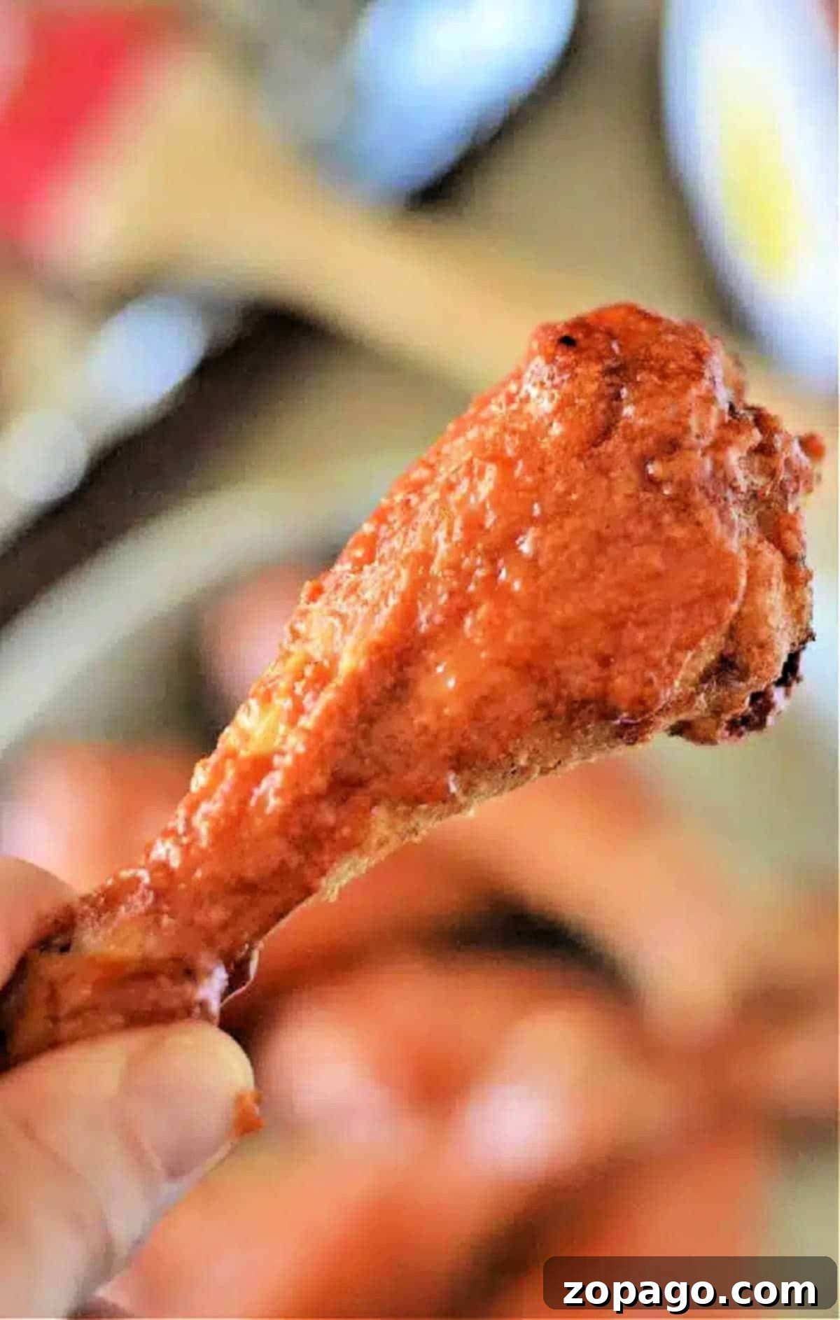 Crispy Baked Chicken Legs 2 A hand holding a crispy, saucy baked chicken leg, reminiscent of buffalo chicken drumsticks, with a blurred background.