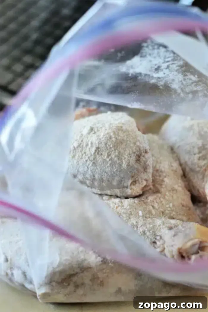 Crispy Baked Chicken Legs 4 An open plastic bag containing raw, floured chicken pieces rests on a kitchen counter. The chicken pieces are coated with flour, ready for further preparation like turning them into delicious baked chicken legs. The background shows a partial view of a dark kitchen appliance.