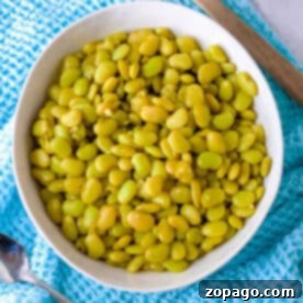 Cooking Dried Lima Beans Perfectly 7 A bowl of perfectly cooked dried lima beans sits invitingly on a blue cloth, with a wooden spoon and a metal spoon nearby.