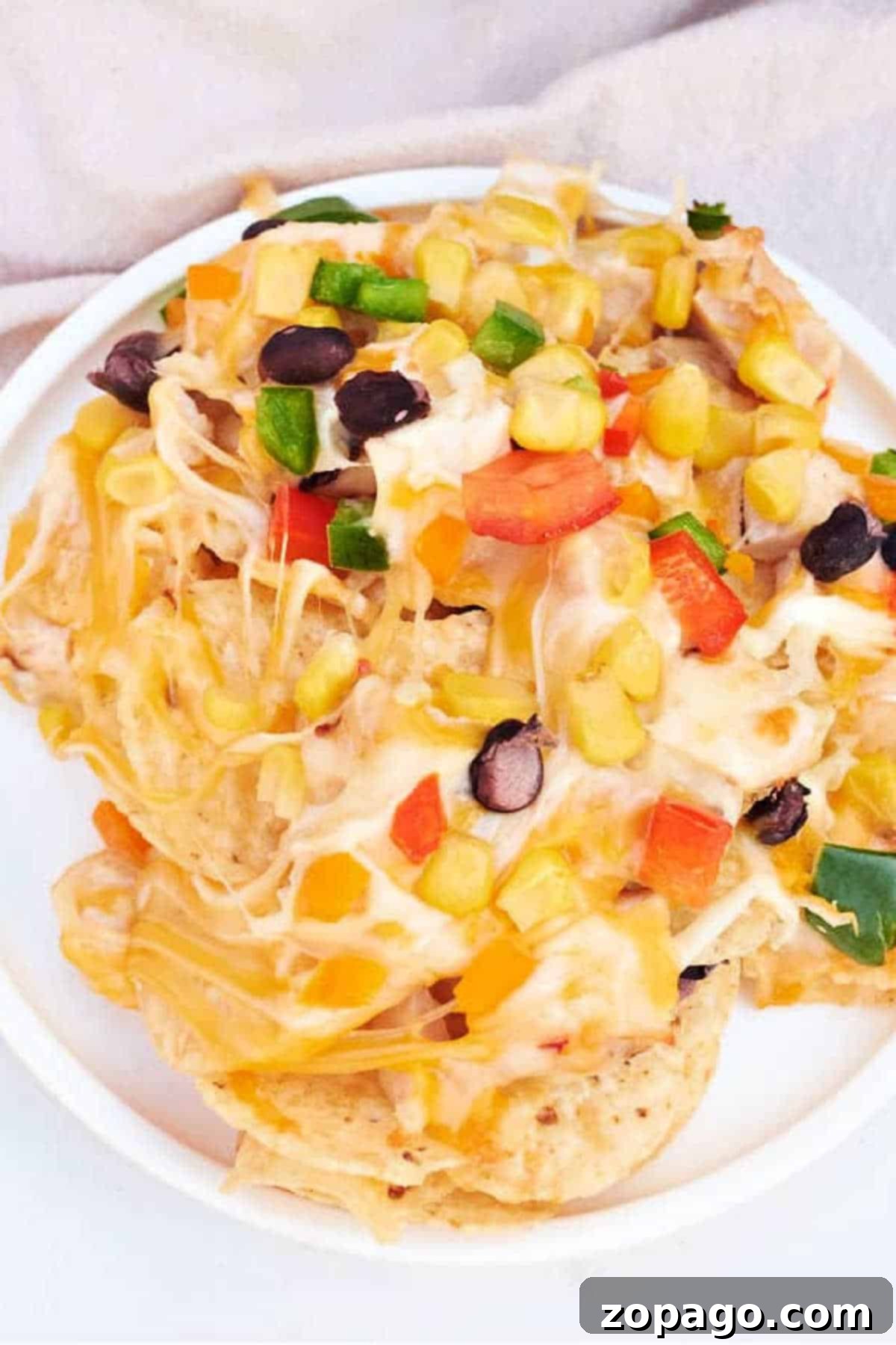 Easy Ninja Foodi Nachos 8 A plate of cheesy ninja foodi Nachos topped with black beans, corn, diced bell peppers, and jalapeños, with a fork digging in.