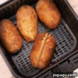 Air Fryer Reheat for Perfect Baked Potatoes 7 Four whole potatoes, with slits on top, are ready to reheat as they sit neatly in the air fryer basket.