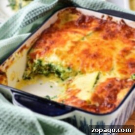 A baked vegetable lasagna with white sauce, sits invitingly in a dish with a piece missing, surrounded by a green towel.