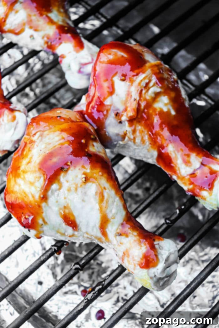 Crispy Smoked Chicken Drumsticks 4 Smoked chicken drumsticks being basted with a vibrant red barbecue sauce on a Traeger grill.