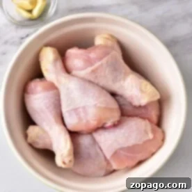 Delicious Chicken Leg Ideas 8 Raw chicken drumsticks in a bowl on a marble surface, accompanied by garlic cloves and a bowl of mayonnaise nearby, ready to inspire the best chicken leg recipes for your next culinary adventure.
