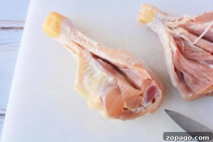 Crispy Oven Butterflied Chicken Legs 3 Two raw chicken drumsticks, expertly butterflied open, resting on a white surface, perfectly prepared for seasoning and cooking.