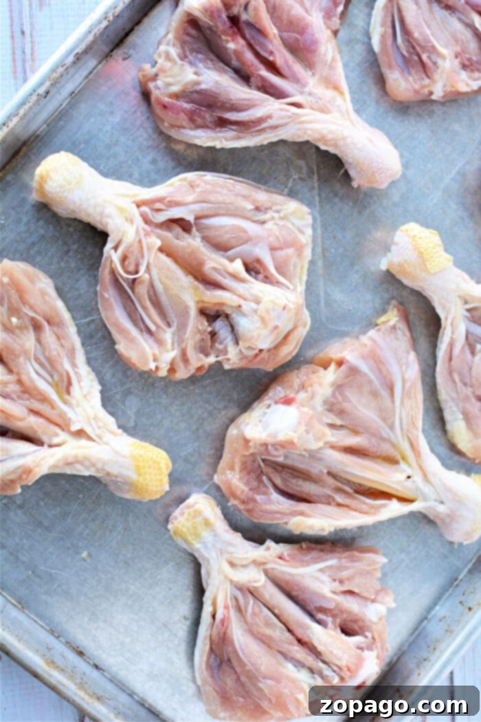Crispy Oven Butterfly Chicken 5 A hand demonstrates the butterflying technique on a raw chicken leg with a sharp knife on a cutting board.