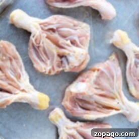 Butterflied chicken legs with skin partially removed are neatly arranged on a metal baking sheet.