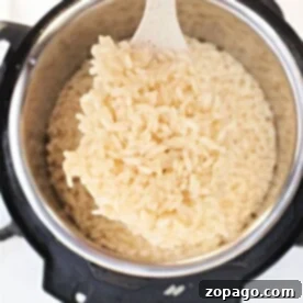 A white spatula lifts perfectly cooked Arborio rice from an electric pressure cooker, demonstrating how to achieve creamy perfection.