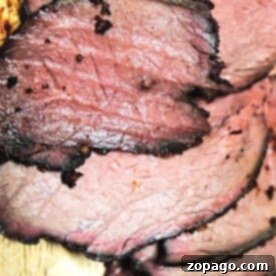 A close-up of several slices of succulent Sirloin Tip Roast, with a browned crust and pink interior, elegantly arranged on a wooden cutting board.