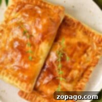 Two golden-brown puff pastries, reminiscent of a classic chicken pot pie, are garnished with thyme on a white plate against a green textured background.