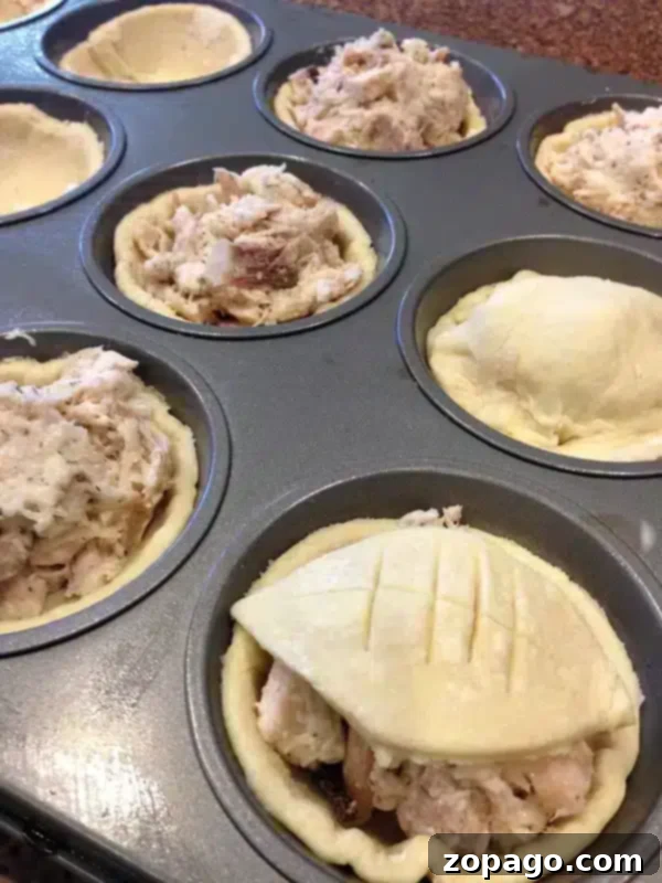 Easy chicken pot pie puff pastry muffin tin dinner idea! It's a great way to use rotisserie chicken or leftover ham or turkey after the holidays are over. Packed with cheese and meat surrounded by flaky puff pastry these chicken bites make for a fun dinner or appetizer during Super Bowl! #chicken #leftover #ham #turkey #puffpastry #appetizer #rotisserie #muffintin #dinner Muffin tin chicken pot pies with puff pastry, some topped with football shapes, served on a white platter.