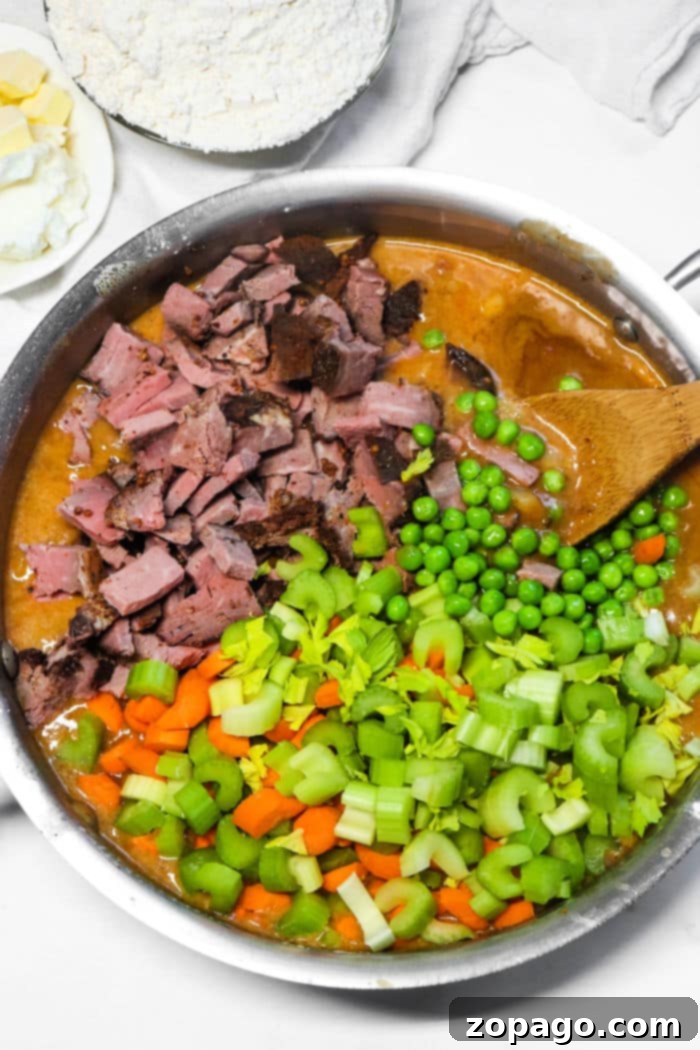 Ultimate Double Crust Pot Pie 3 A pot filled with beef ingredients: chopped beef, peas, carrots, celery, and sauce with a wooden spoon, reminiscent of flavors found in a classic double crust pot pie.