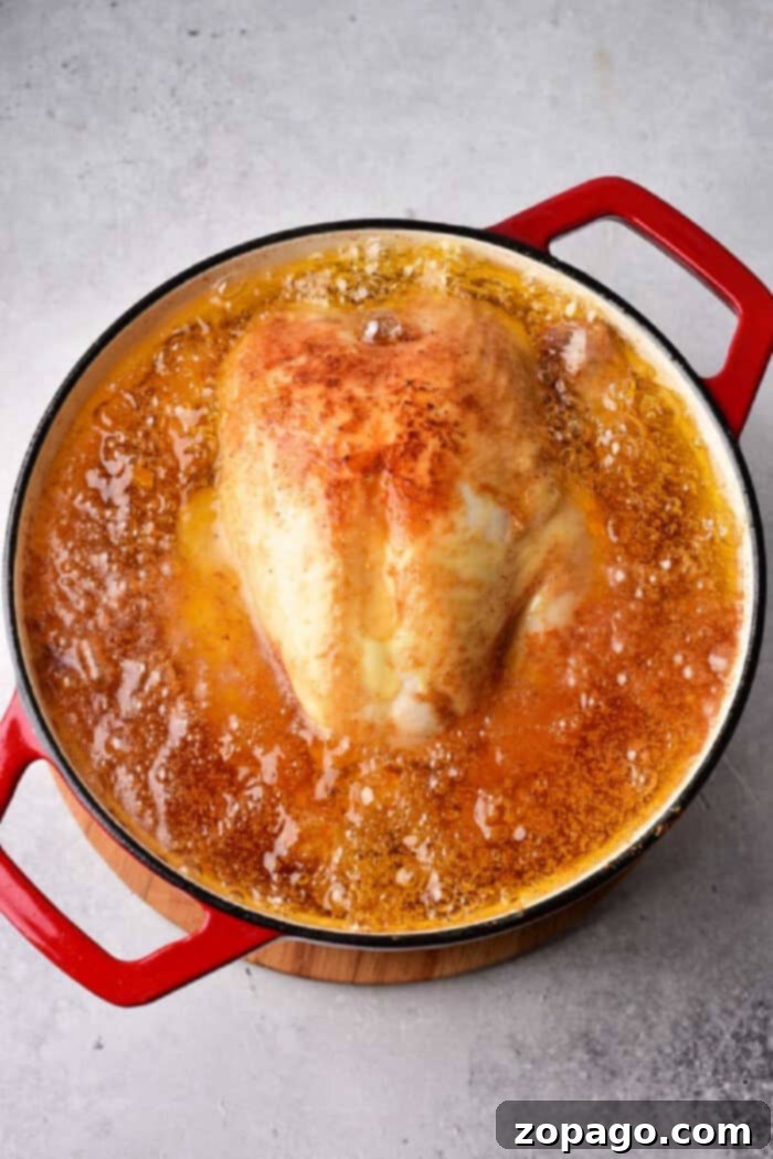 Crispy Whole Fried Chicken 4 A whole fried chicken simmering in a pot of bubbling oil, viewed from above.