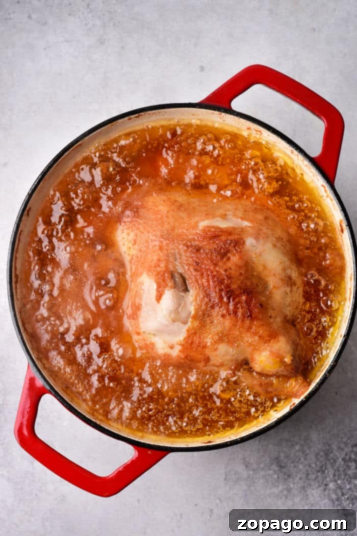 Crispy Whole Fried Chicken 5 A whole fried chicken simmers in a red pot, enveloped in a rich golden-brown oil.