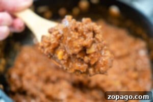 Close-up of a wooden spoon holding a spoonful of cooked, saucy ground beef mixture