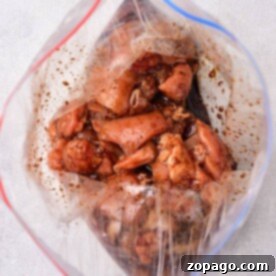Raw marinated chicken pieces, perfect for your favorite stir fry recipes, rest in a clear plastic ziplock bag on a light gray surface.