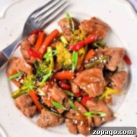 Savor the delicious Chicken Thigh Stir Fry featuring tender chicken, broccoli, bell peppers, and sesame seeds artfully arranged on a white plate with a fork.