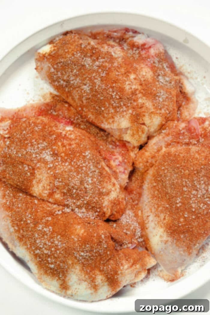 Raw chicken breasts generously coated with a rich, reddish dry rub, ready for smoking on a Traeger grill.