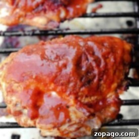 Smoked chicken breast covered in barbecue sauce is grilling on the barbecue grate, showcasing a delicious charred exterior.
