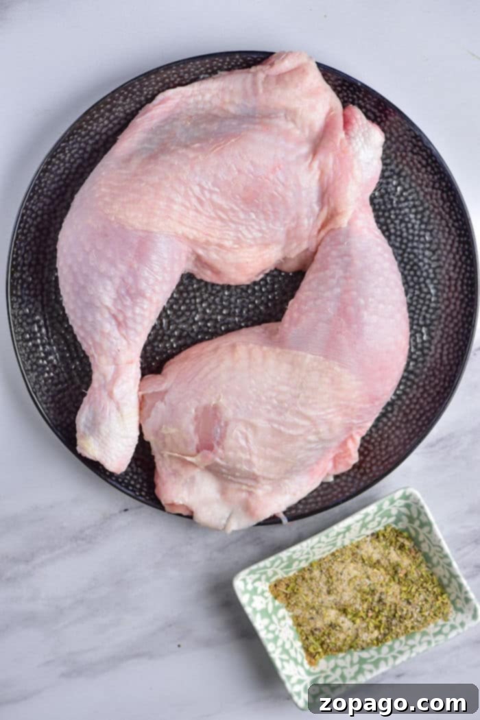 Perfect Chicken Leg Quarters 4 Raw chicken quarters rest invitingly on a black plate, accompanied by a small dish of spices on the marble surface—your first step in mastering how to cook chicken leg quarters to perfection.