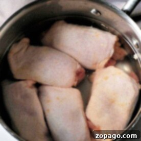 Raw chicken thighs sit in a stainless steel pot, preparing for the next step—wondering how long to boil chicken thighs for the perfect tenderness.