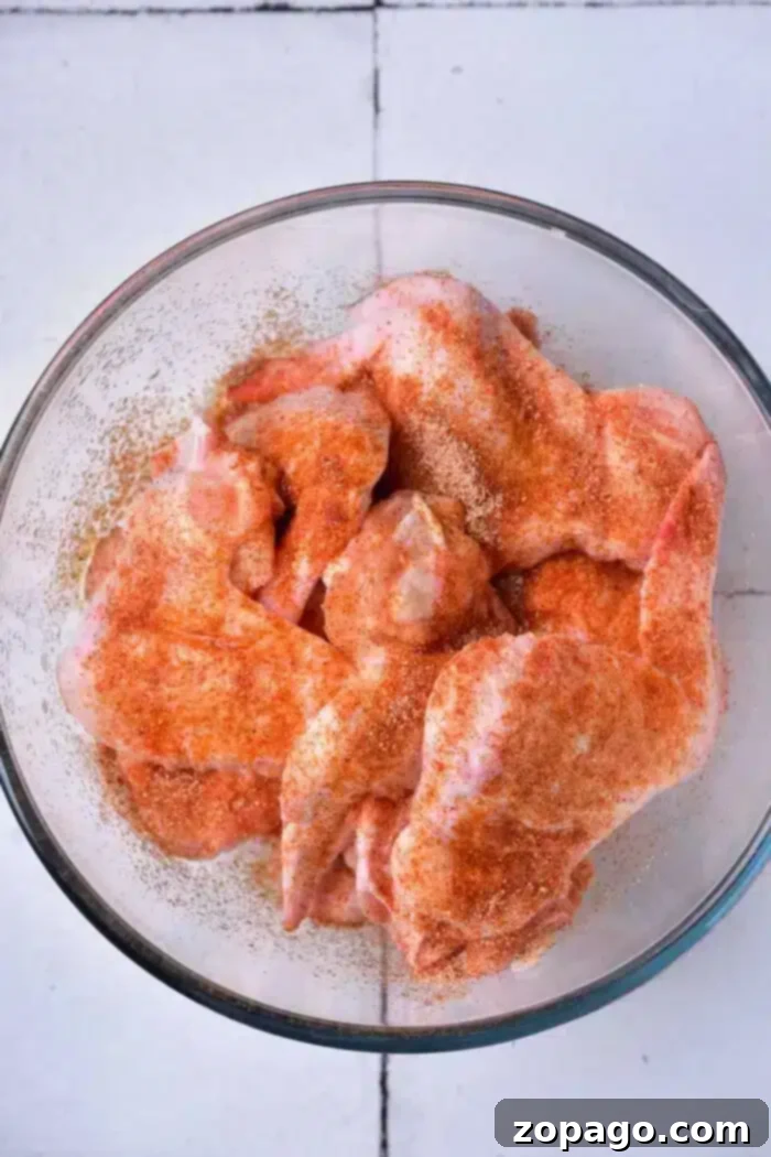 Crispy Baked Whole Chicken Wings 4 A glass bowl containing raw chicken wings, seasoned with a reddish spice mix, ready to be transformed into delicious baked whole chicken wings, sits on a white tiled surface.