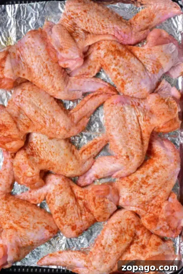 Crispy Baked Whole Chicken Wings 5 Raw, seasoned whole chicken wings neatly arranged in a single layer on a foil-lined baking sheet, ready for the oven.