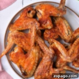 A plate of delicious, baked whole chicken wings rests on a white surface, invitingly crispy and surrounded by the soft color of a pink cloth nearby.