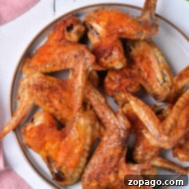 A plate of delicious, baked whole chicken wings rests on a white surface, invitingly crispy and surrounded by the soft color of a pink cloth nearby.