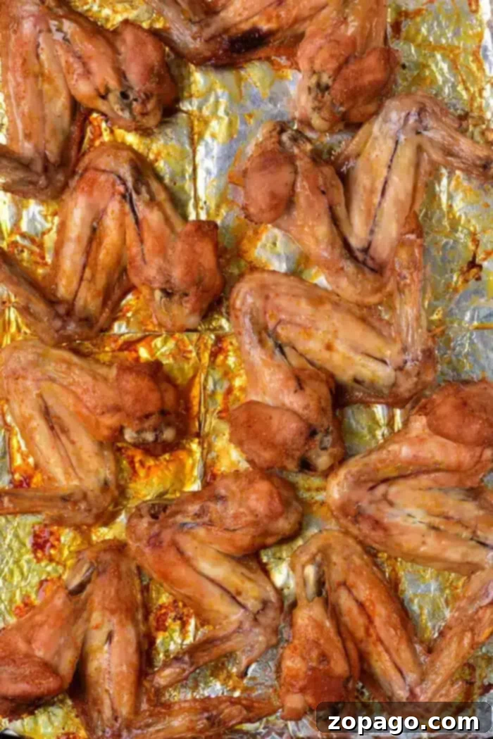 Crispy Baked Whole Chicken Wings 7 A baking sheet filled with perfectly baked whole chicken wings, arranged in rows on a foil-lined tray, golden brown and crispy.