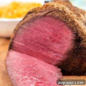 Close-up of a sliced Top Round Roast Recipe, featuring a crispy crust on a wooden board. Sides are blurred in the background.