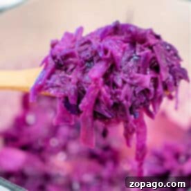 A wooden spoon holding sauteed red cabbage over a pot filled with more shredded cabbage.