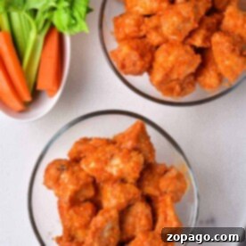 Bowls of spicy buffalo chicken bites with celery and carrot sticks arranged on a pristine white surface.