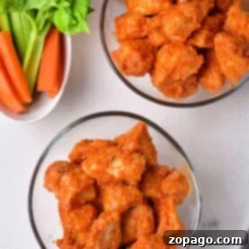 Bowls of spicy buffalo chicken bites with celery and carrot sticks arranged on a pristine white surface.