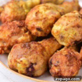 Golden brown curry fried chicken drumsticks stacked on a white plate.