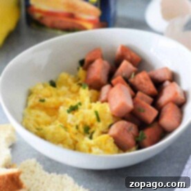 A bowl of scrambled eggs and cubed Spam, with a Spam can in the background, brings the classic flavor to life—your ideal Spam and Eggs recipe.