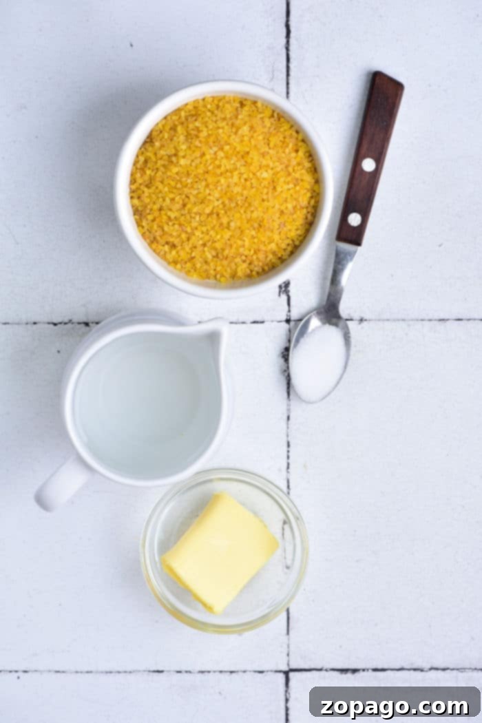 Fluffy Bulgur Every Time 3 Ingredients for cooking bulgur: a bowl of bulgur, a pitcher of water, a glass dish of butter, and a spoonful of salt on a white tiled background.