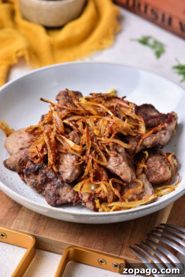 Perfect Chicken Liver Dishes 2 A plate of grilled chicken liver topped with crispy fried onions sits on the table, tempting you to pick up the nearby fork. This dish perfectly complements a guide on how to cook chicken liver to perfection.