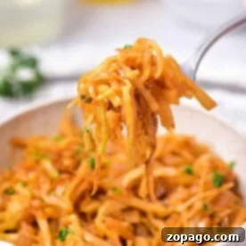 A fork holds a portion of sautéed shredded cabbage, perfectly embodying an Indian cabbage recipe, above a white bowl filled with more savory goodness. The dish is garnished with chopped herbs. In the blurred background, white bowls and clear bottles subtly enhance the scene.