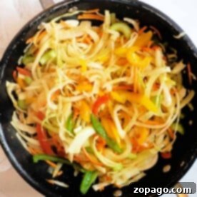 A skillet filled with sautéed mixed vegetables, featuring bell peppers, onions, and zucchini, takes inspiration from a Jamaican Cabbage Recipe.