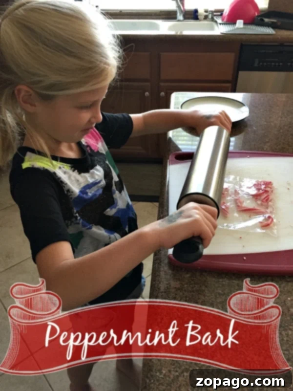 Easy peppermint bark recipe. This no bake peppermint bark is the easiest way to make this Christmas dessert with kids! #peppermintbark #peppermint #dessert #christmas A young girl is using a rolling pin to crush peppermint candy pieces on a cutting board in a kitchen. The text "Microwave Peppermint Bark" is shown at the bottom of the image with a decorative ribbon banner.