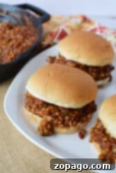 Three Sloppy Lentil Joes sit on a white plate beside a skillet, all resting on a woven mat.