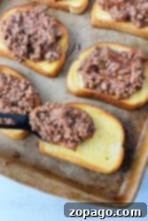 Ultimate Texas Toast Sloppy Joes 10 Texas toast sloppy joes come to life as a ground beef mixture rests atop hearty slices of bread on a baking tray. A spatula carefully places one portion, readying this classic, savory delight guaranteed to satisfy appetites.