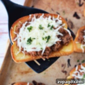 A slice of Texas toast topped with savory meat sauce and melted cheese, garnished with parsley, sits enticingly on a spatula over a baking sheet.