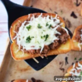 A slice of Texas toast topped with savory meat sauce and melted cheese, garnished with parsley, sits enticingly on a spatula over a baking sheet.